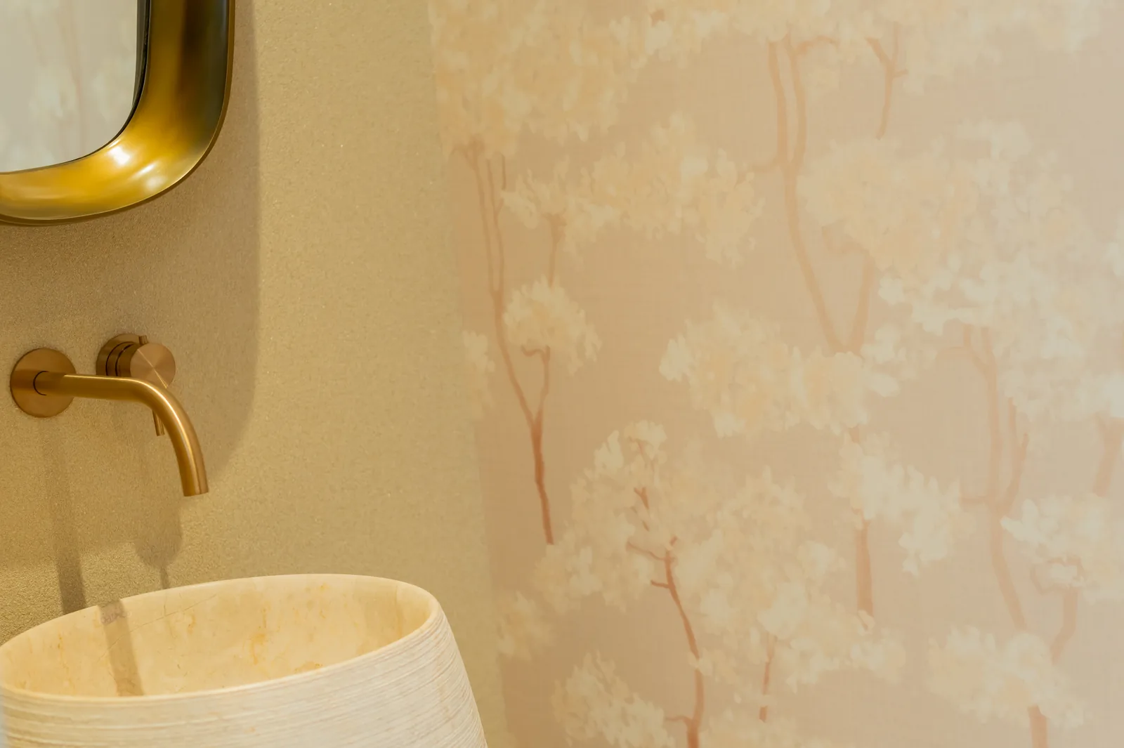 Aseo de cortesía con lavabo de piedra, grifería en oro y papel pintado de motivo floral