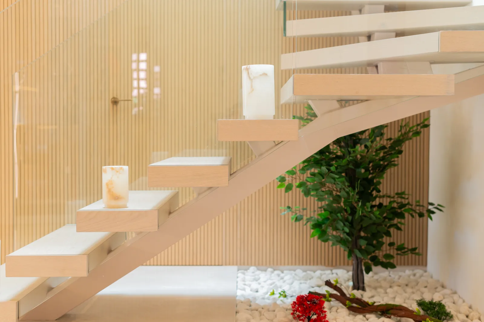 Escalera de peldaños volados de madera con velas de alabastro, panel de listones y jardín de grava
