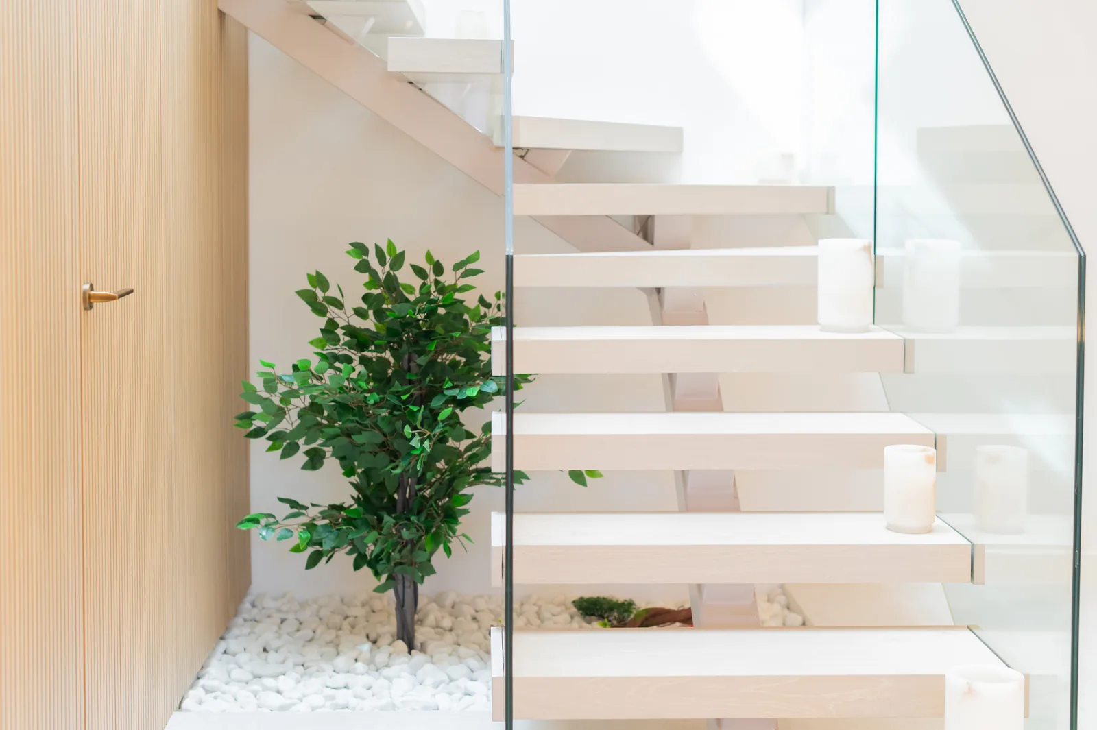 Escalera de peldaños volados de madera con barandilla de vidrio junto a jardín interior de grava blanca