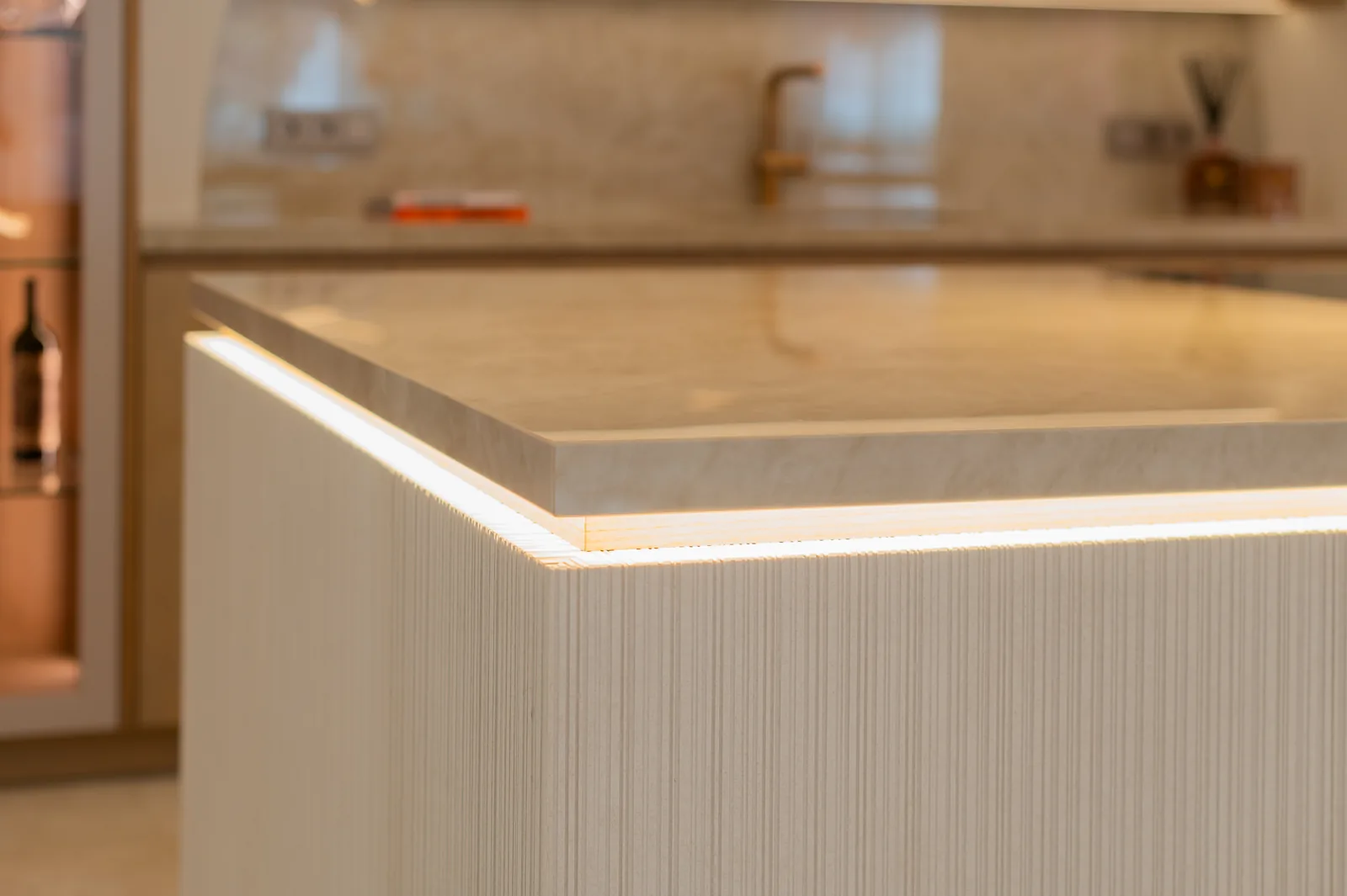 Esquina de isla de cocina con encimera de mármol y tira LED perimetral bajo el canto