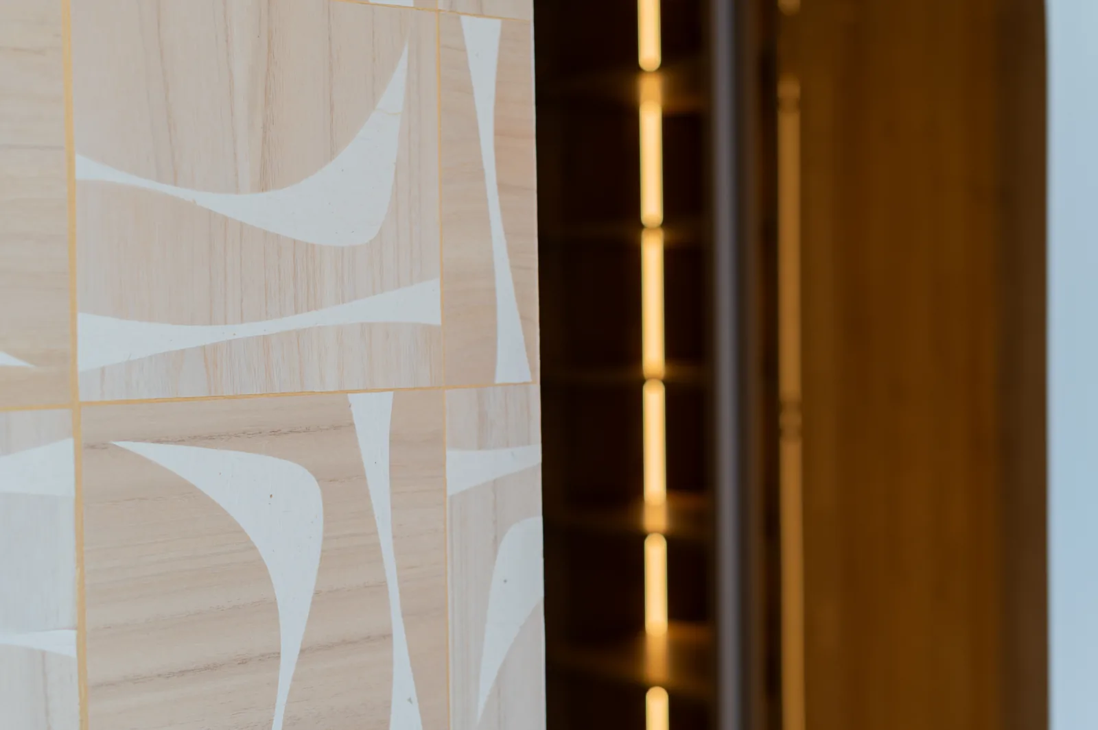 Panel de marquetería en madera clara con motivo geométrico junto a vitrina con iluminación LED