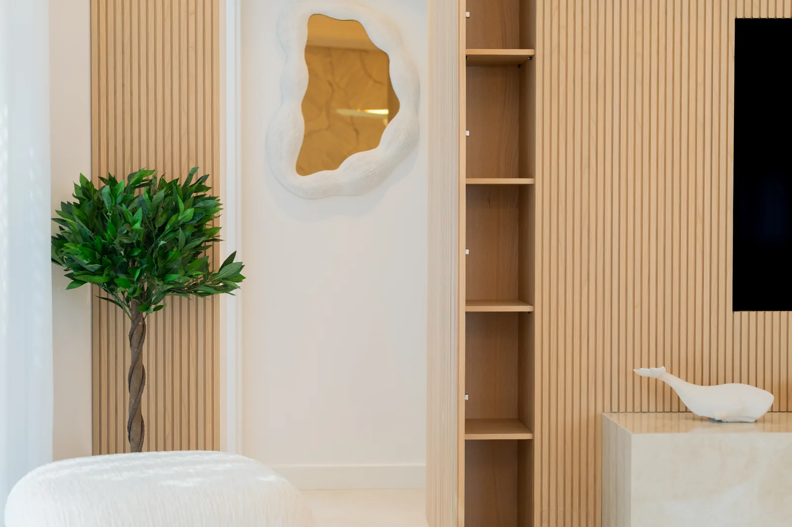 Recibidor con espejo de forma orgánica, estantería abierta y paneles de listones de madera