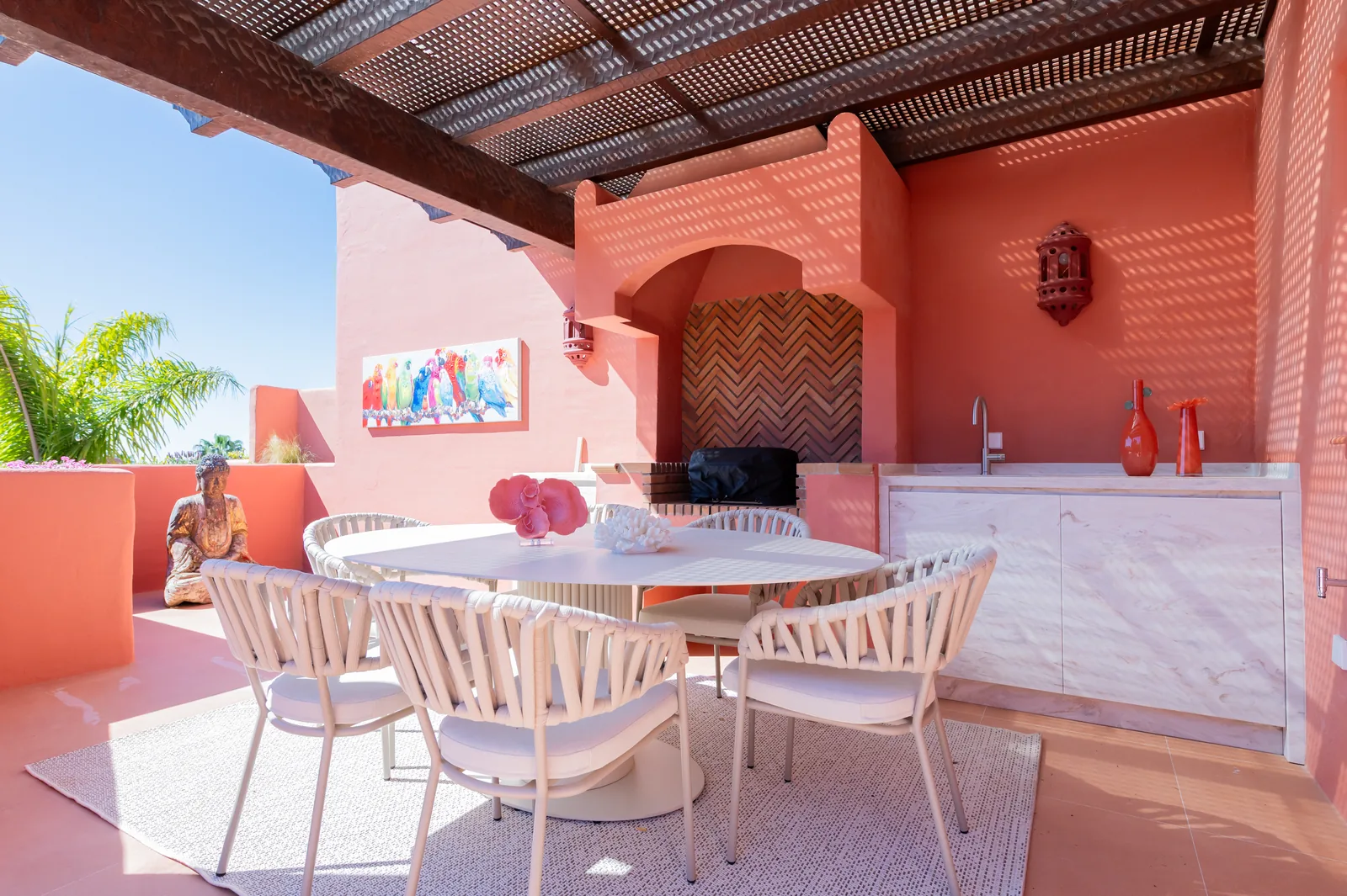 Terraza con pérgola de madera, comedor exterior y paredes en tono coral con barbacoa de obra